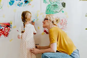 Adult and child painting together on an indoor wall.