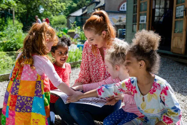 Adult reading a book with a small group of children outdoors.