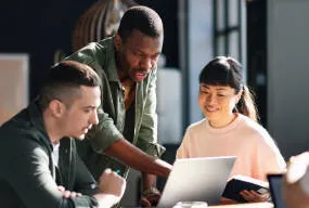 Three adults working together at a laptop.