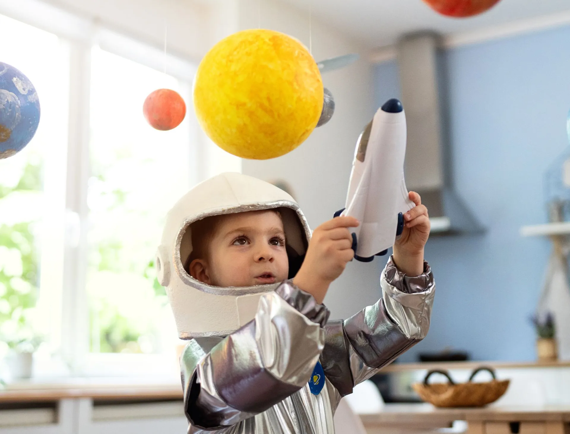 Child in an astronaut costume holding a toy rocket indoors.